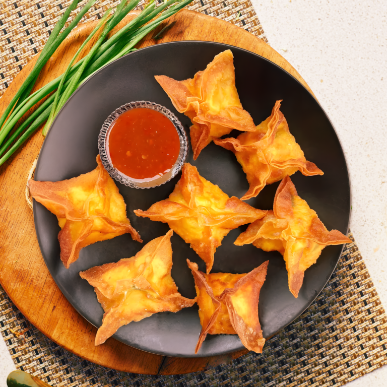 Golden fried crab rangoons served with Thai sweet chili sauce on a black plate.