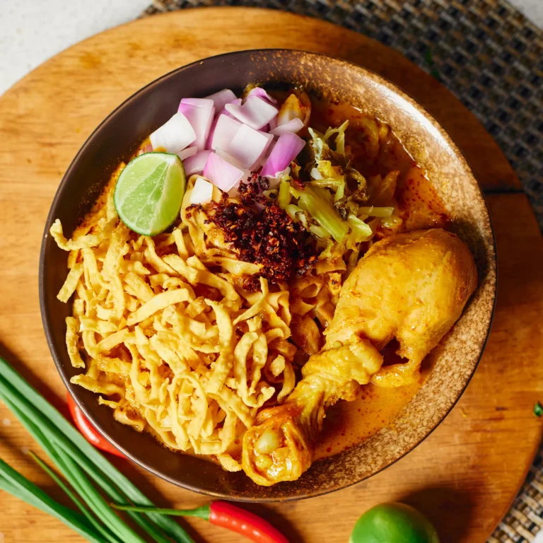 Creamy Northern Thai curry noodle soup with chicken drumstick, crispy noodles, pickled mustard greens, shallots, and lime