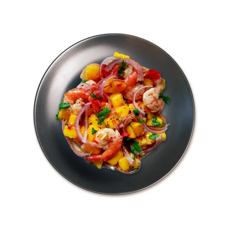 Colorful mango shrimp salad with red onions, fresh herbs, and chili on a dark plate