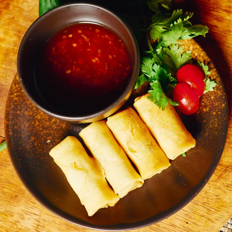 Golden crispy spring rolls served with sweet chili sauce, garnished with cilantro and cherry tomatoes