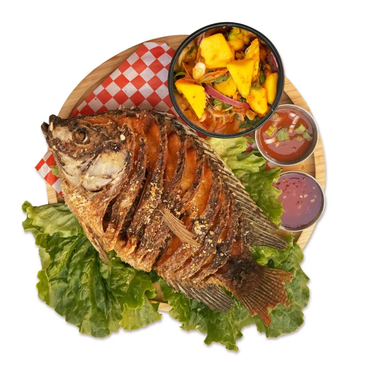 Crispy whole tilapia served with spicy mango salad and Thai dipping sauces on a wooden platter